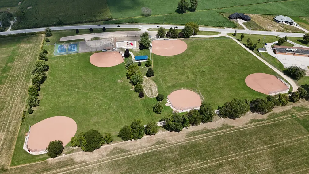 Aerial view of park showing baseball diamonds, pavilion, playground, and sports courts 