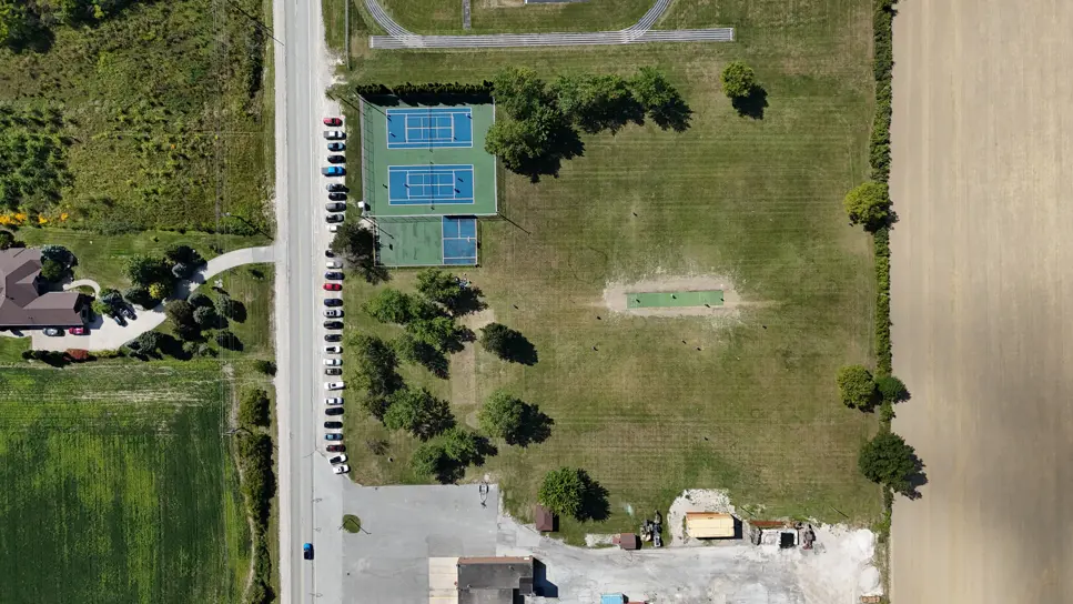 Image shows high level view of current conditions of the park, including tennis/pickleball courts, basketball court, cricket pitch and trees