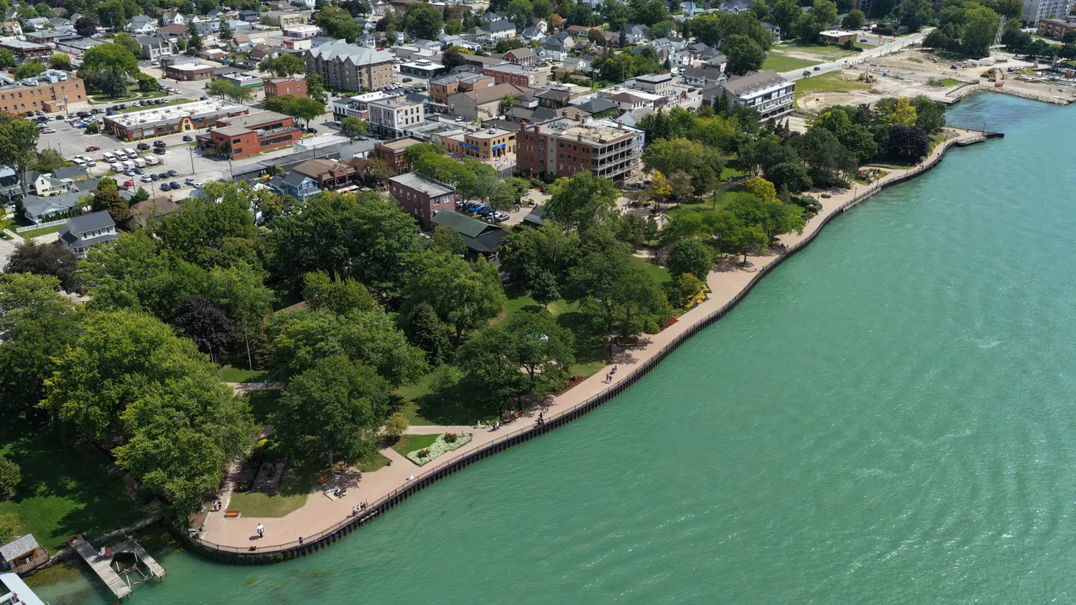 High aerial view of park looking back towards the town, showing waterfront, trail, trees and buildings