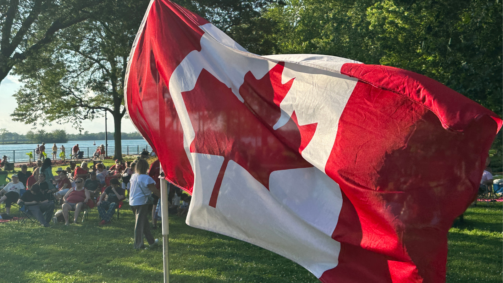 Canadian flag waving in the wind with the park and river behind