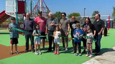 People standing in front of playground equipment at Malden Centre Park cutting a green ribbon signifying the opening of the playground