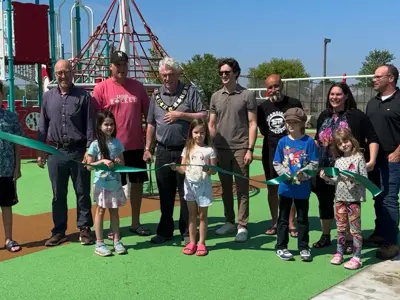 People standing in front of playground equipment at Malden Centre Park cutting a green ribbon signifying the opening of the playground