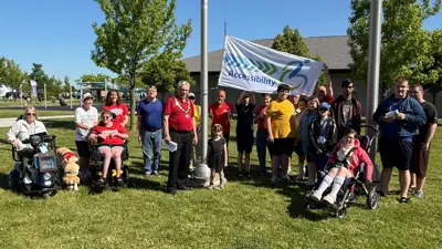 Members of the community pose with the County of Essex accessibility flag in front of the Libro Centre fieldhouse. Flag poles are in the background