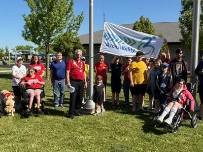 Members of the community pose with the County of Essex accessibility flag in front of the Libro Centre fieldhouse. Flag poles are in the background