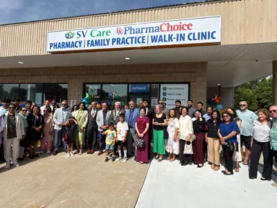 A large group of people stand for a photo below a sign for a new medical facility in Amherstburg. SV Care Medical & Walk-in-Clinic