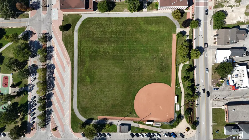 Aerial view of park showing baseball diamond, pathway, parking and washroom building.