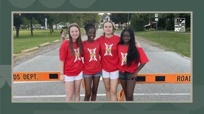 Four girls wearing red Canada Day shirts pose for a photo in front of a road closure during an event