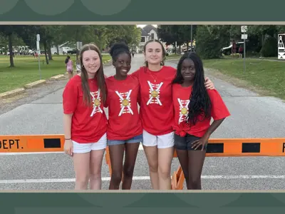 Four girls wearing red Canada Day shirts pose for a photo in front of a road closure during an event