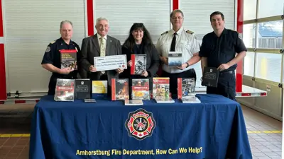 Three members of Amherstburg Fire Department alongside the Mayor and a representative from Enbridge standing in front of training books