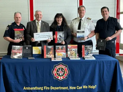Three members of Amherstburg Fire Department alongside the Mayor and a representative from Enbridge standing in front of training books
