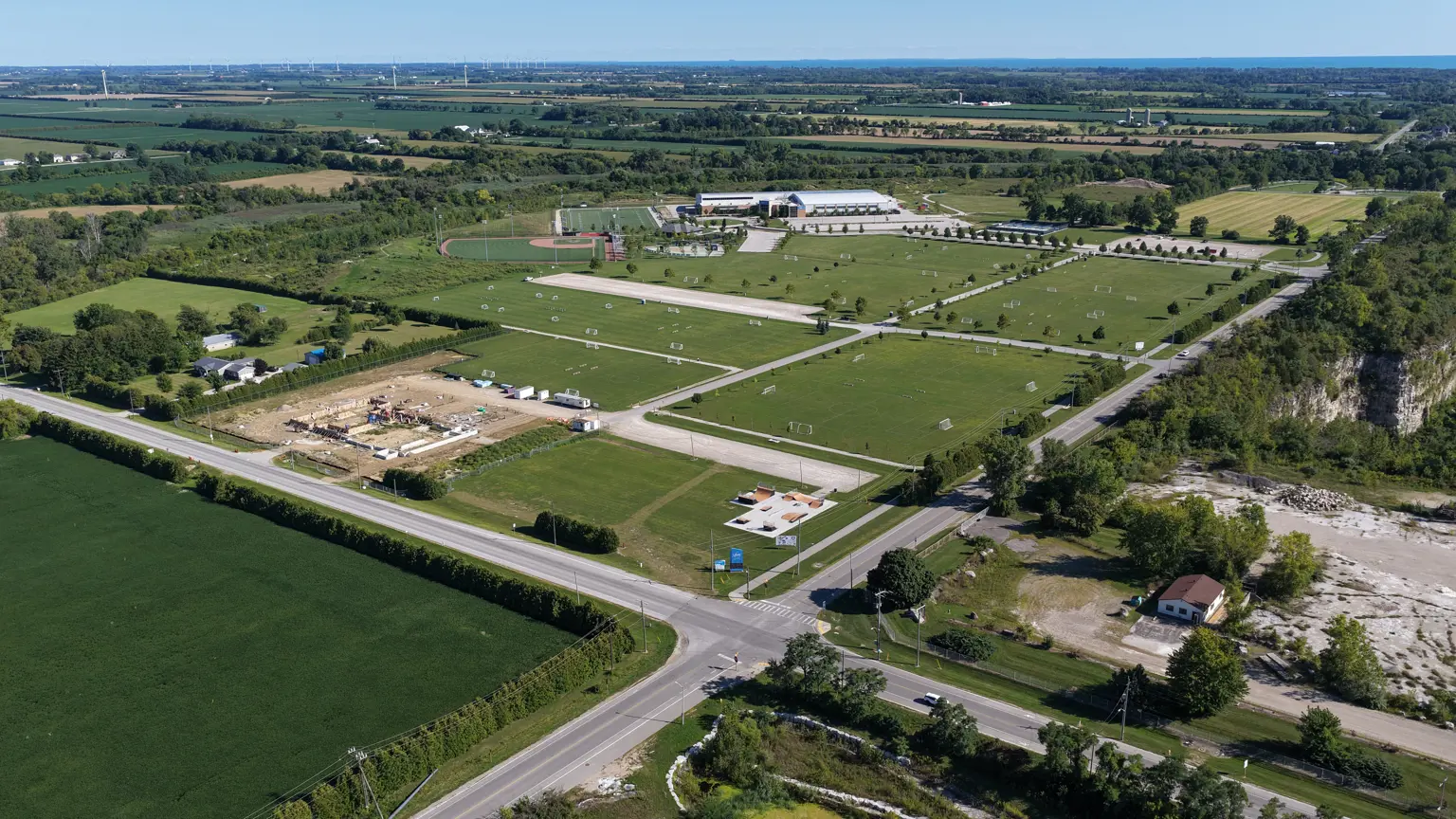 Aerial image of park from the corner of Meloche Rd and Simcoe St showing the skatepark, soccer fields, roadways, along with premier baseball diamond and outdoor soccer/football field and Libro Credit Union Recreation Complex. Construction of the new Fire Station 1 is also shown.