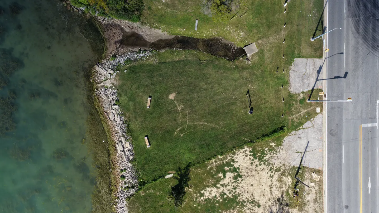 Aerial overview of park showing rocks at waterfront, 2 benches and grassed area.